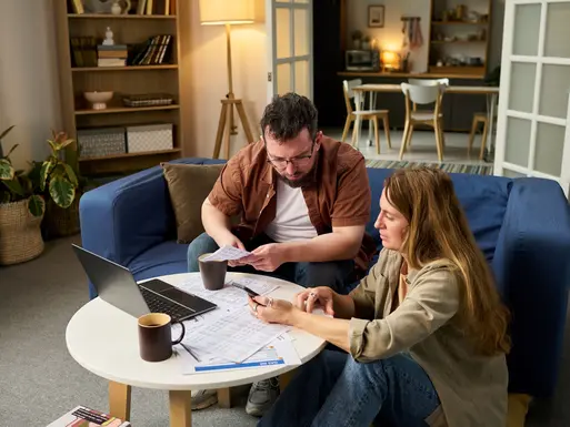 Man and woman reviewing financial documents and using laptop together at home